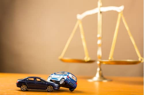 Toy car crash and justice scales, concept of Milledgeville car accident lawyer