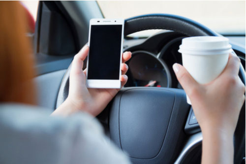 driver holding phone and cup, Atlanta distracted driving accident lawyer concept
